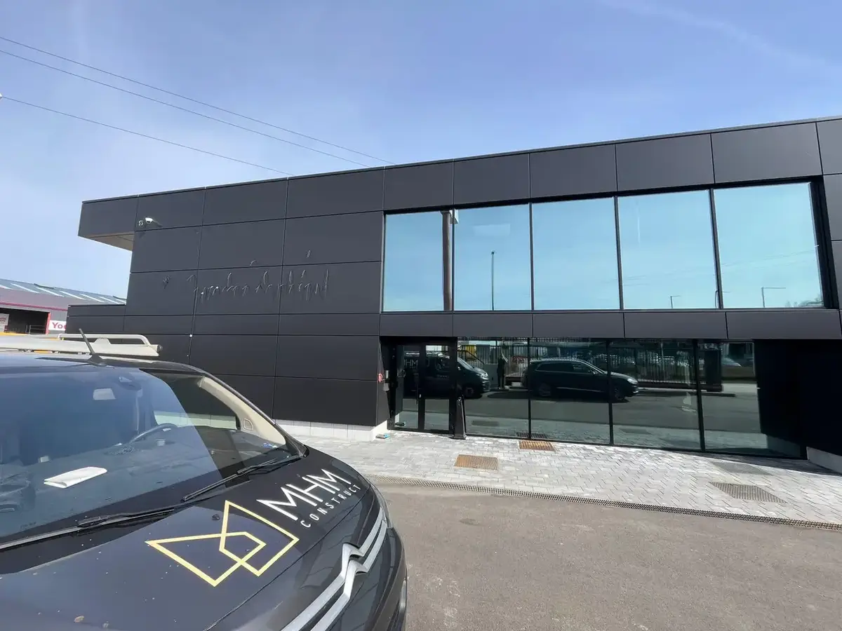 Bâtiment à façade en panneaux noirs et grandes baies vitrées, avec la camionnette MHM Construct au premier plan
