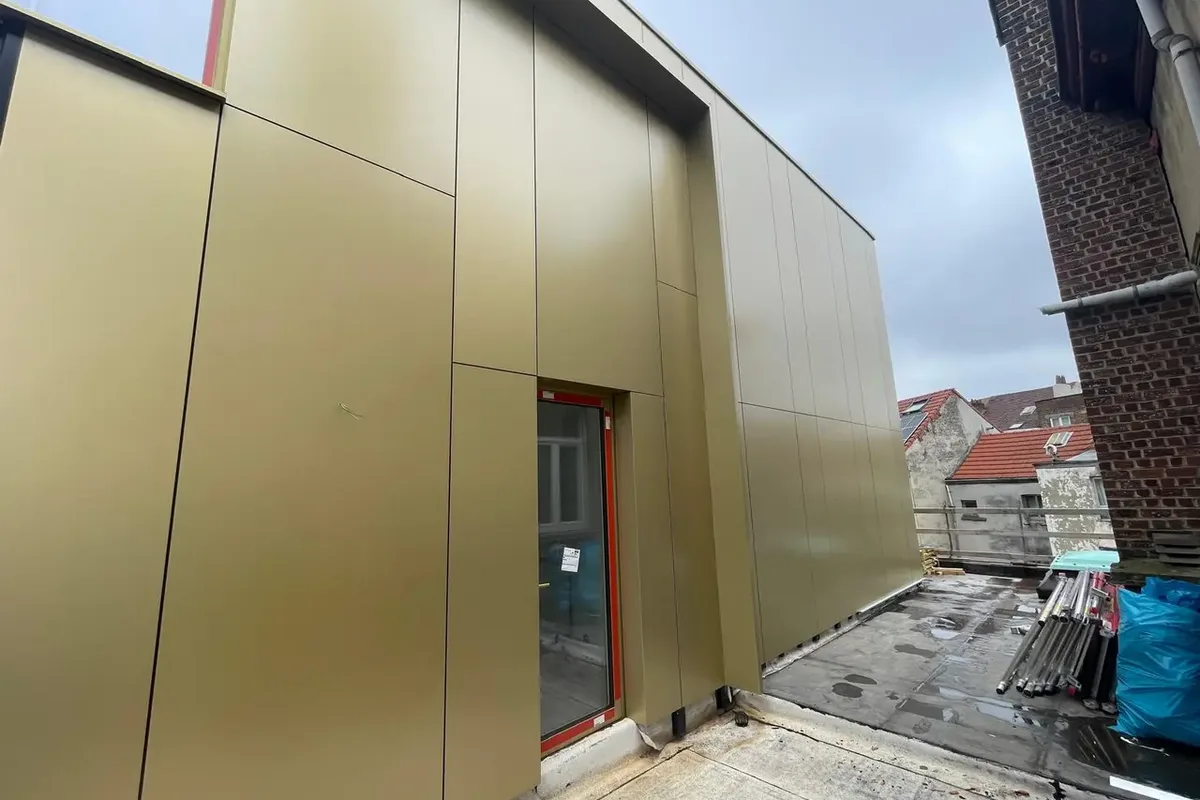 Façade en panneaux d'aluminium doré séparés par des joints, avec une porte à cadre rouge