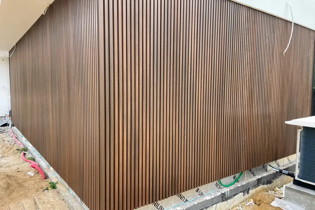 Grand mur habillé de lames de bois verticales en claire-voie, avec un pare-pluie visible en pied de façade