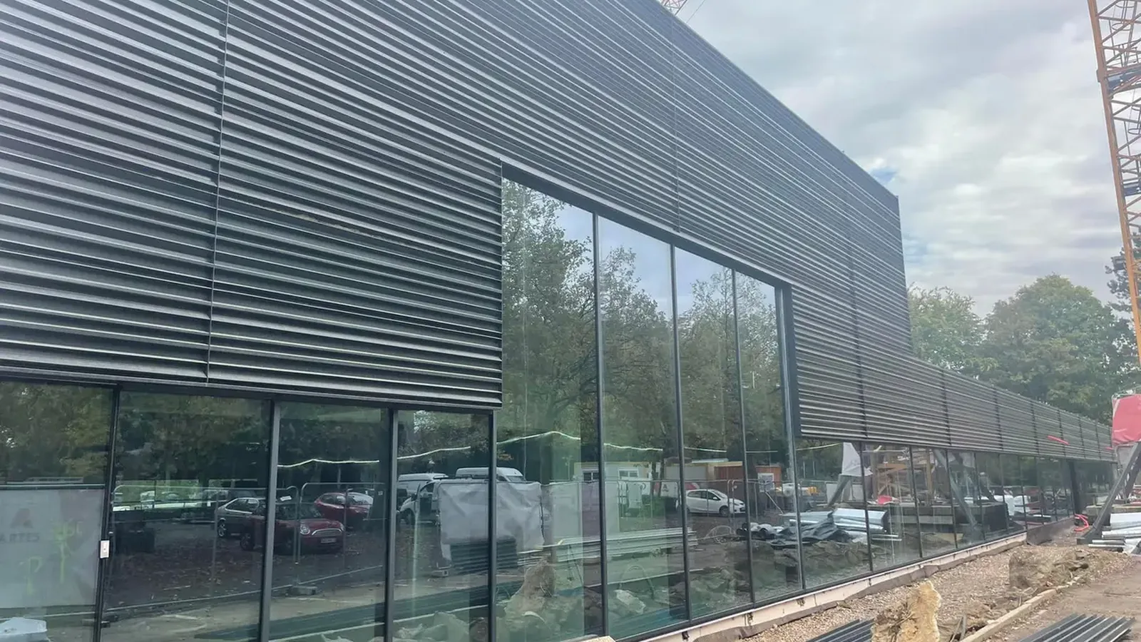 Grand bâtiment professionnel habillé de bardage métallique sombre nervuré, avec une longue baie vitrée