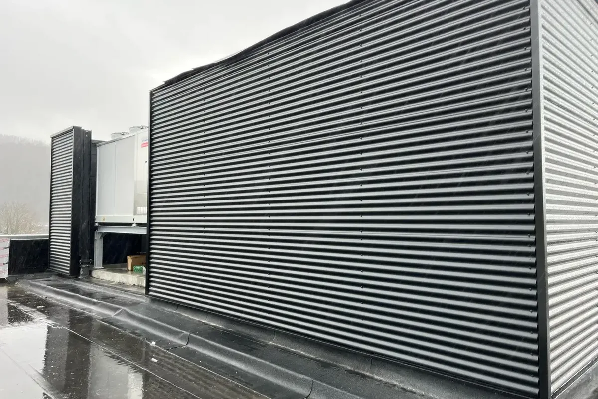 Grand pan de bardage métallique nervuré gris anthracite au-dessus d'une toiture plate