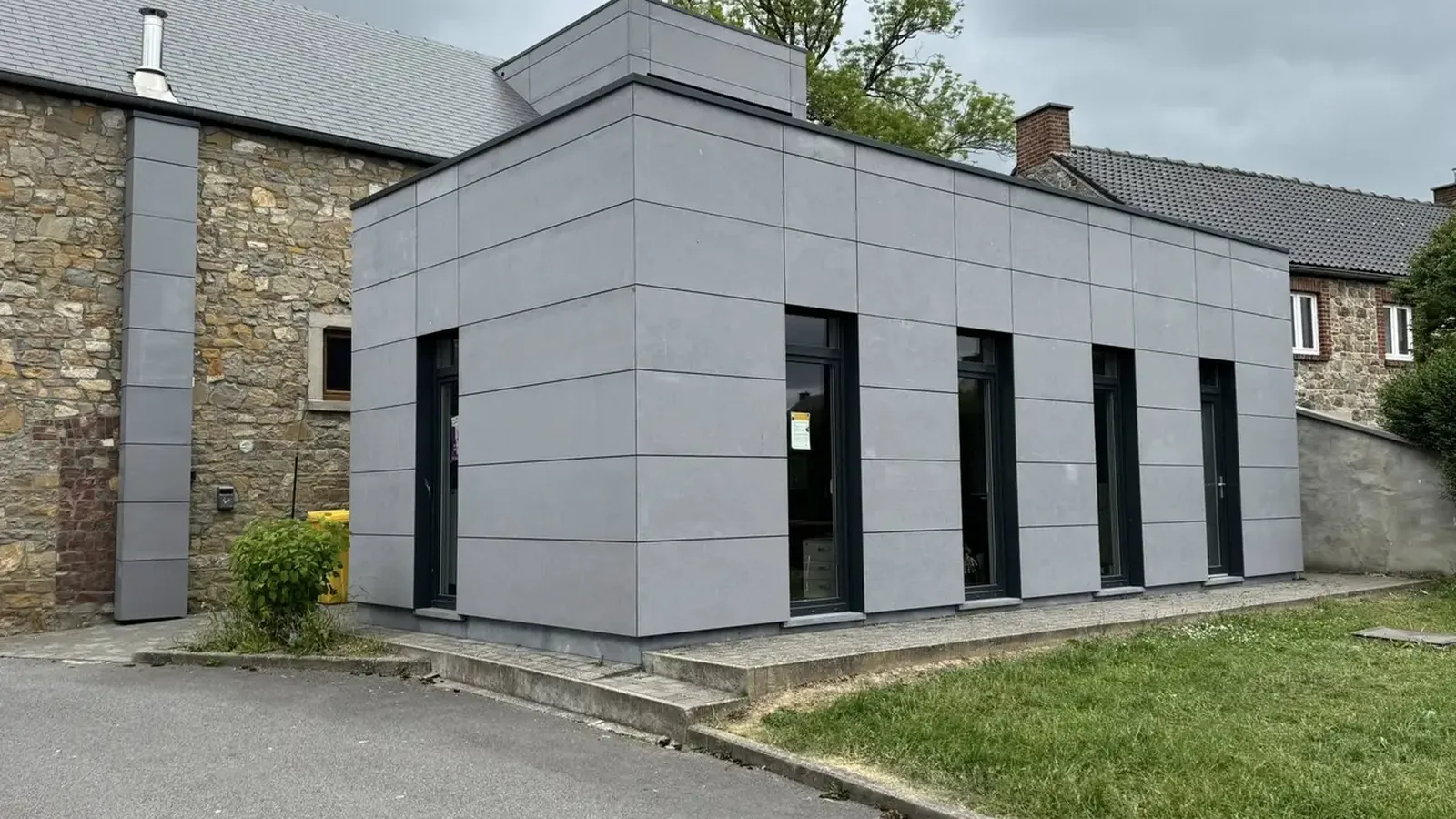 Extension en panneaux gris à côté d'un bâtiment ancien en pierre au toit d'ardoises