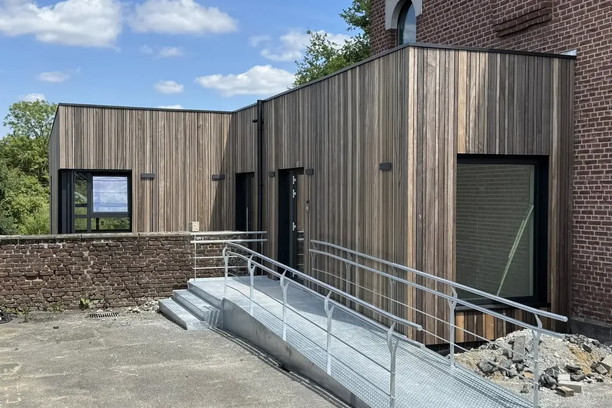 Annexe en bardage de bois à côté d'un bâtiment en briques, avec une rampe d'accès