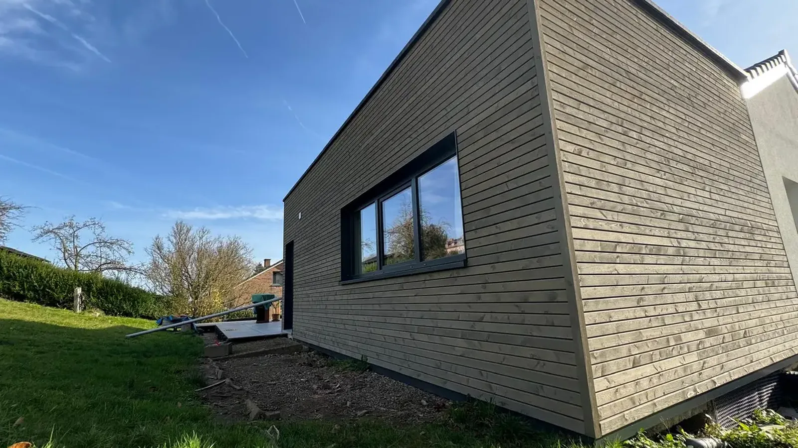 Maison basse habillée de lames de bois grisées par le temps, au bord d'une pelouse