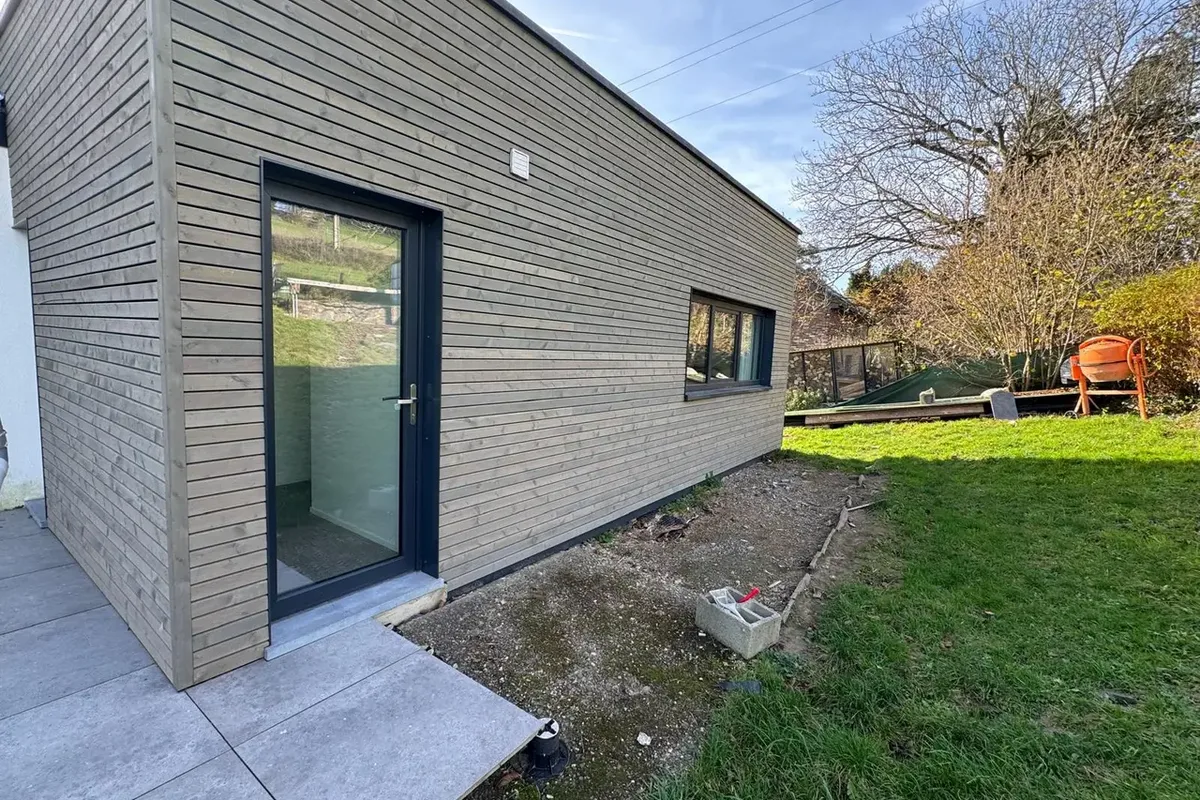 Pied de façade en bois grisé avec une porte vitrée et des dalles propres au sol