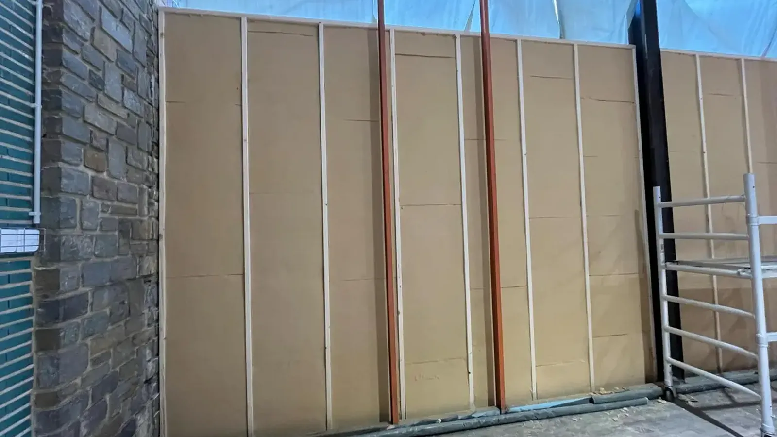 Mur recouvert de panneaux isolants en fibre de bois fixés sur tasseaux, avec un échafaudage roulant à droite