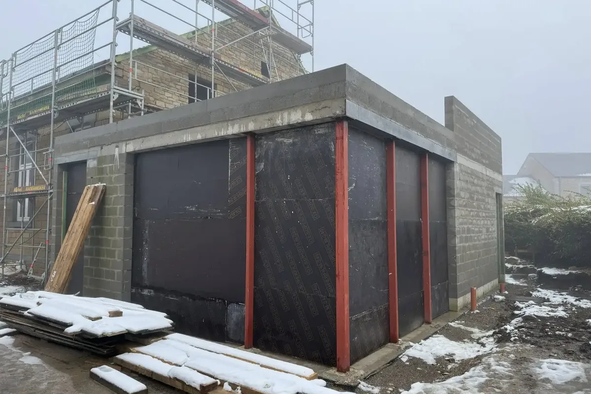 Mur de blocs recouvert d'une membrane noire, montants rouges et neige au sol