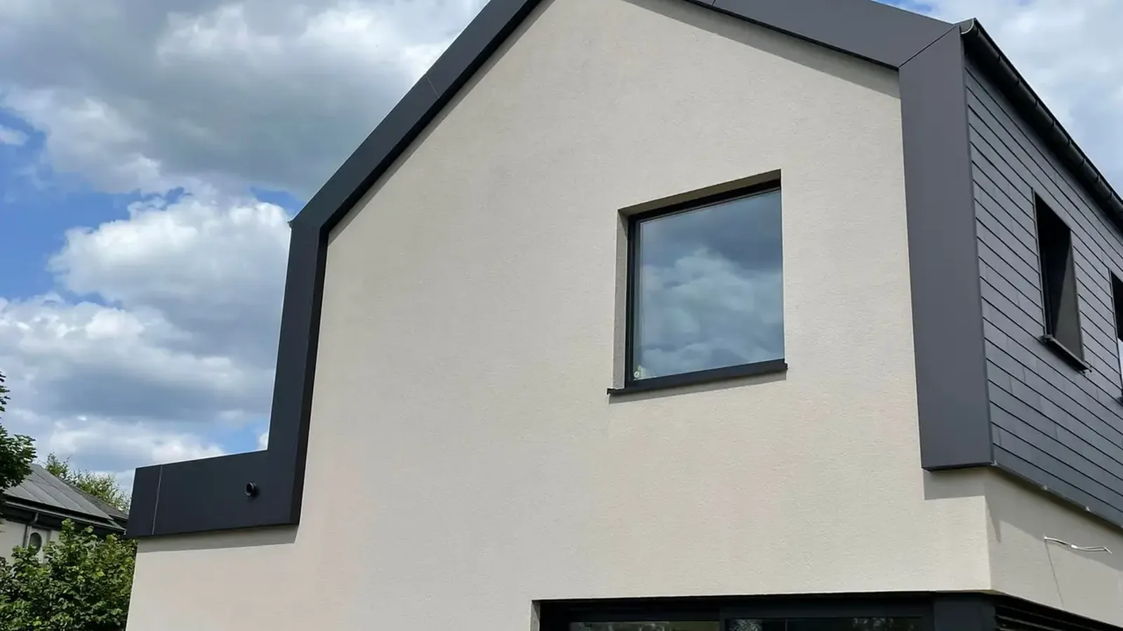 Maison à façade enduite blanc cassé, avec un liseré anthracite en bordure de toiture