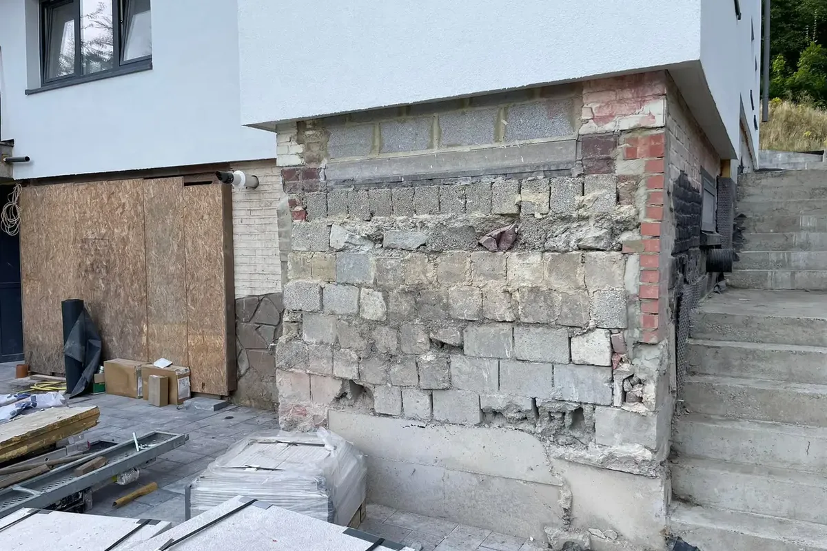 Mur ancien en pierres et briques en cours de réfection au pied d'une façade enduite, avec un escalier à droite