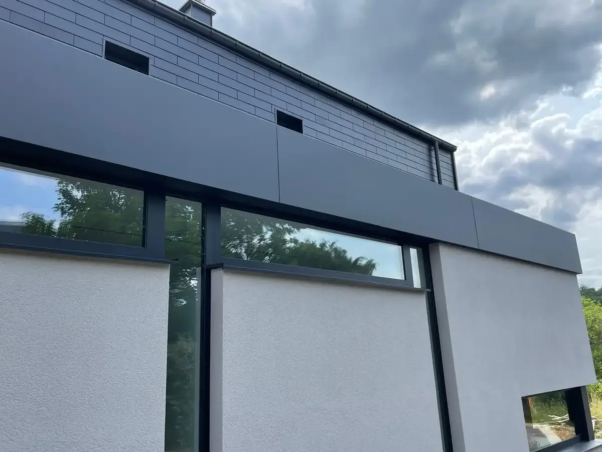 Façade enduite grise surmontée d’un bandeau de bardage anthracite au-dessus des fenêtres